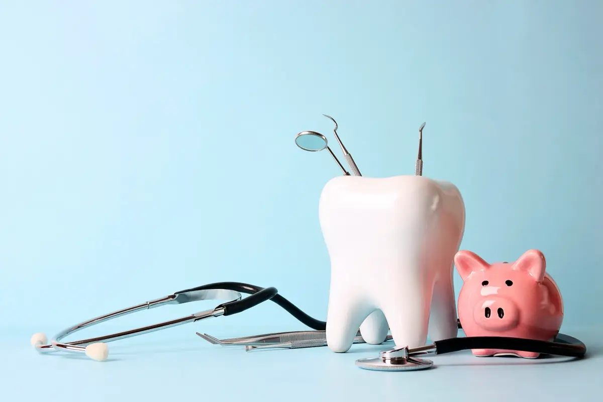 A model tooth with dental instruments and a savings bank, representing the cost of dental care.